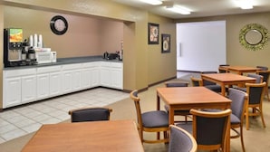 Une chambre d’hôtel équipée d’une kitchenette, d’un coin repas avec des tables et des chaises en bois, et d’une horloge au mur.