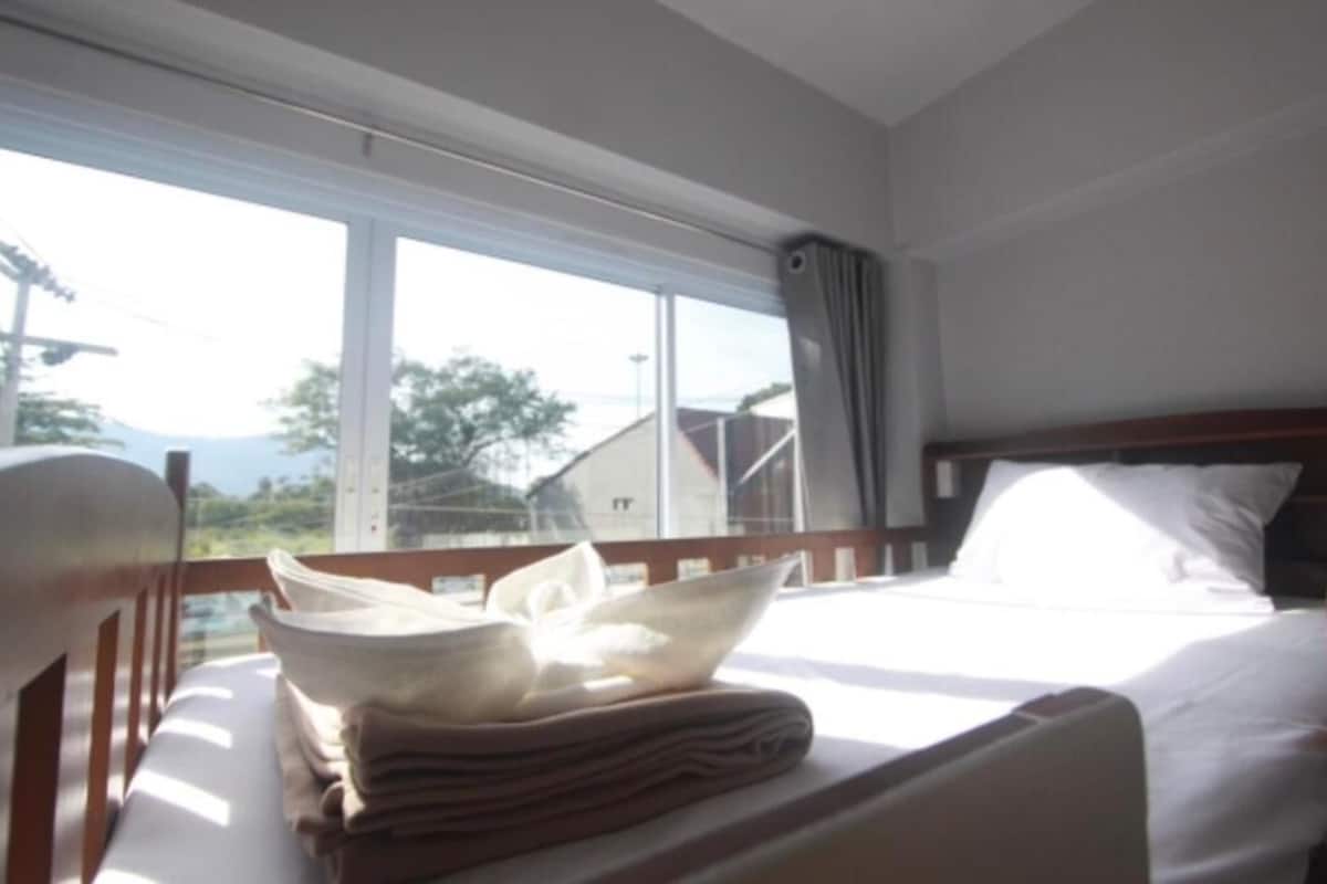 A hotel room with a bed, a window with curtains, and a view of the outside.