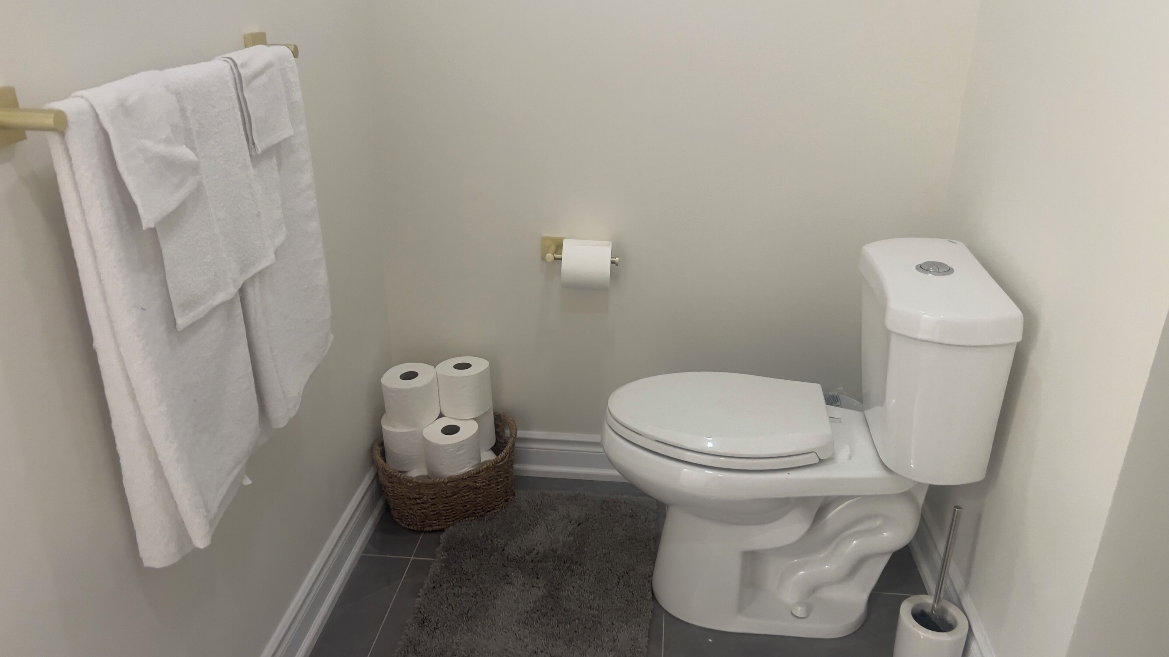 Un baño con un inodoro blanco, un rollo de papel higiénico en la pared, una cesta con papel higiénico y una toalla colgada en un perchero.