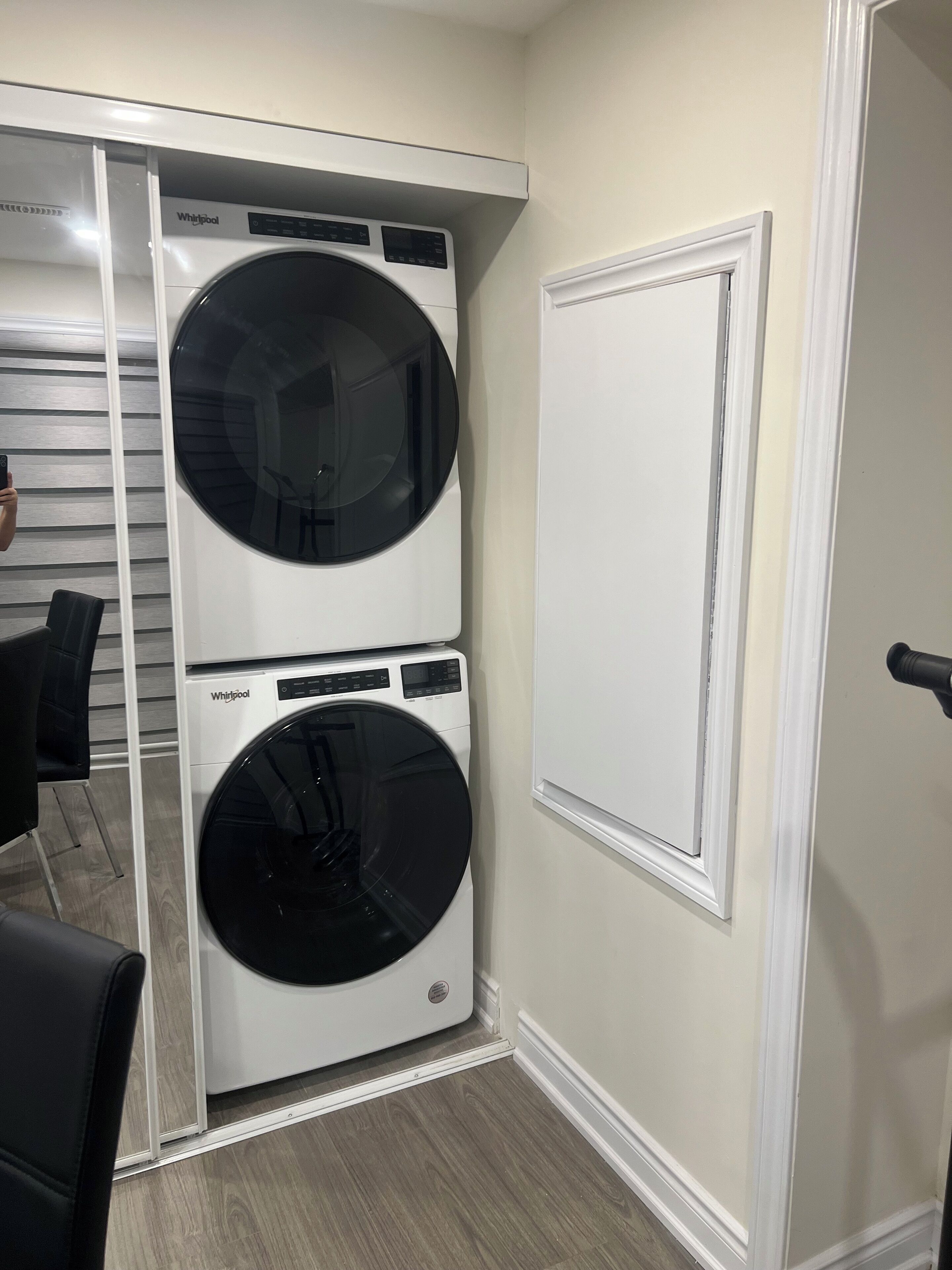 Una lavandería con dos lavadoras y secadoras apiladas, una puerta blanca y suelo de madera.