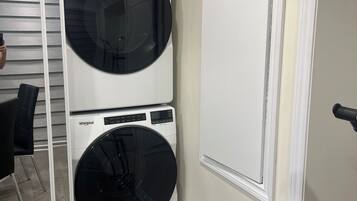 Una lavandería con dos lavadoras y secadoras apiladas, una puerta blanca y suelo de madera.