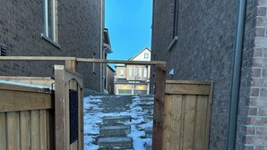 A narrow alleyway with wooden gates and steps leading to a brick building. - The Luxe Haven (East Gwillimbury)