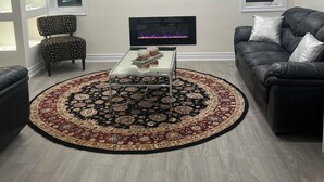 A modern living room with a flat-screen TV, a patterned armchair, a leather sofa, and a decorative rug. - The Luxe Haven (East Gwillimbury)