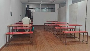 Μια αίθουσα διδασκαλίας με ξύλινο δάπεδο, κόκκινα θρανία και ένα άτομο που κάθεται μπροστά.