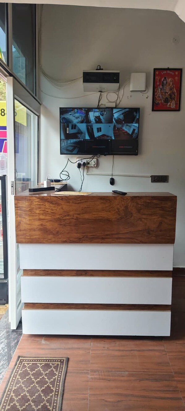 Una recepción con encimera de madera y cajones blancos, un televisor de pantalla plana montado encima y una unidad de aire acondicionado en la pared.