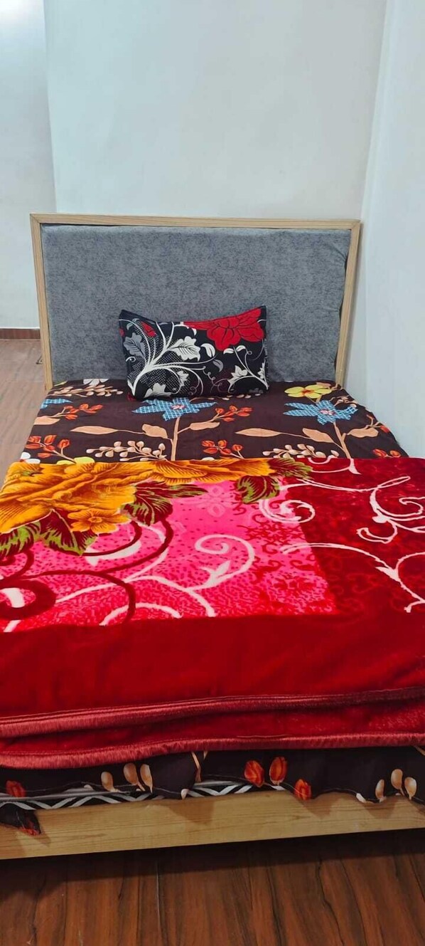 A bed with a floral-patterned bedspread, a grey upholstered headboard, and a single decorative pillow. - Hotel Sky View (Dehradun)