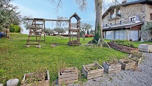 Un espace extérieur rustique doté d’aires de jeux en bois, d’un bâtiment en pierre avec un balcon et de jardinières surélevées.