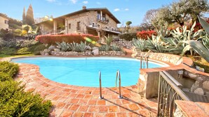 A swimming pool with a stone deck, surrounded by landscaped gardens and a stone house.