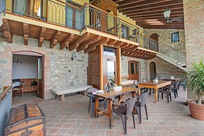 Un patio al aire libre con muros de piedra, vigas de madera y una mesa de madera con sillas.