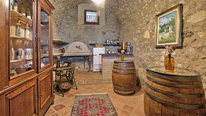A rustic kitchen with stone walls, wooden cabinets, a vintage sewing machine, a wooden barrel, and a stone fireplace.