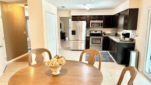 A modern kitchen with dark cabinets, stainless steel appliances, and a dining area with a wooden table and chairs. - Pool Party in Daytona! Sleeps 8 (Holly Hill)