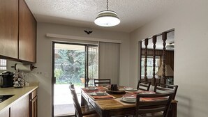 Zona pranzo con tavolo in legno apparecchiato per quattro persone, circondato da sedie. Una finestra offre vista su spazi verdi.
