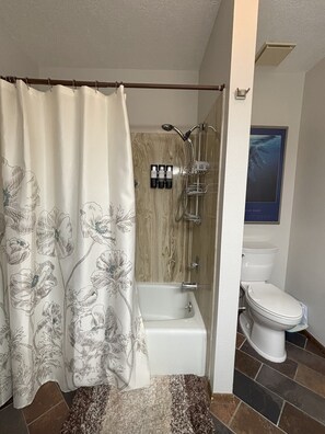 A bathroom with a shower curtain, a bathtub, a toilet, and a wooden wall.