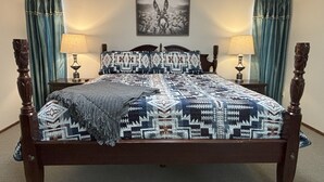 Un letto con una coperta a motivi, due abat-jour, un quadro appeso al muro e tende alle finestre.