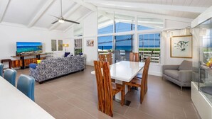 A spacious living area with a dining table, chairs, and a sofa. There is a large window offering a view of the ocean. - Butterfly House:  Beautiful Ali'i Drive Home with Ocean Views! (Kailua-Kona)