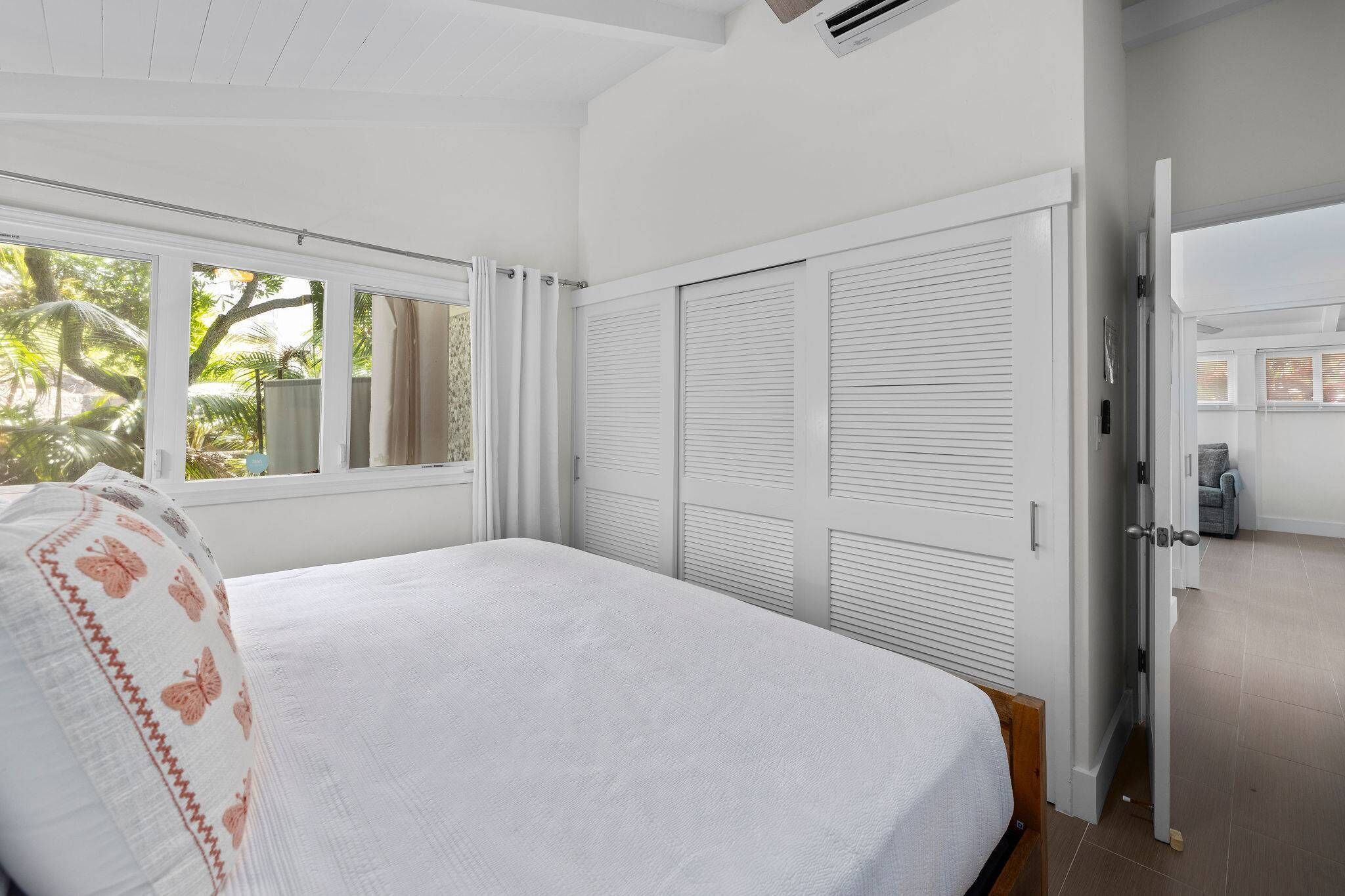 A bedroom with a bed, white curtains, a window, and a wardrobe.