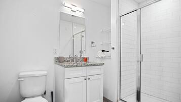 Un bany modern amb un vàter blanc, un lavabo amb taulell de granat, una cabina de dutxa de vidre i parets revestides de rajoles blanques.