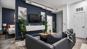A modern living room with a grey sofa, a flat-screen TV, and two potted plants. - CozySuites - William (Pittsburgh)