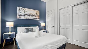 A bedroom with a large bed, two bedside tables with lamps, a painting on the wall, and a set of white doors.