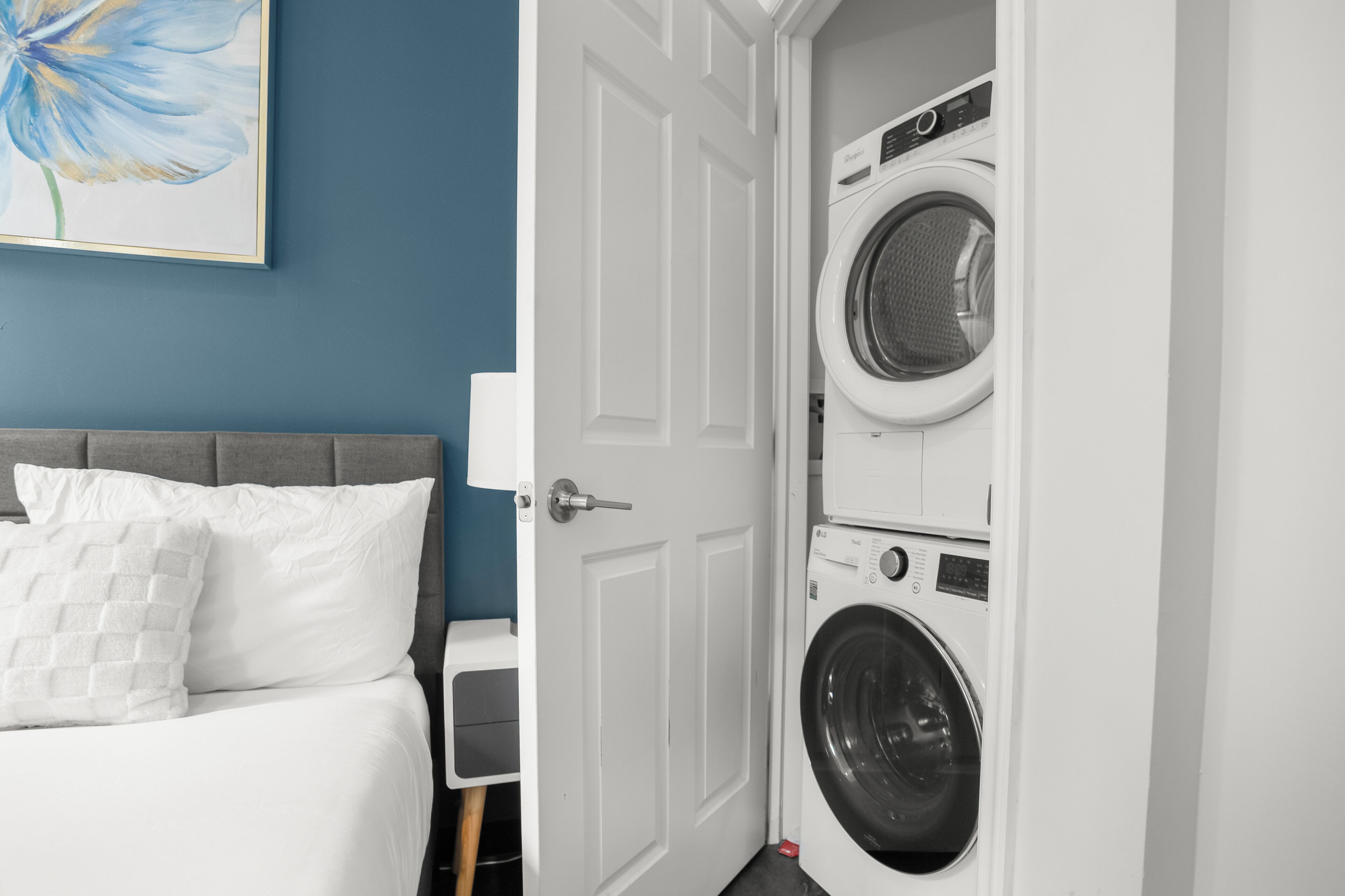A hotel room with a bed, a washing machine, and a door leading to another room.