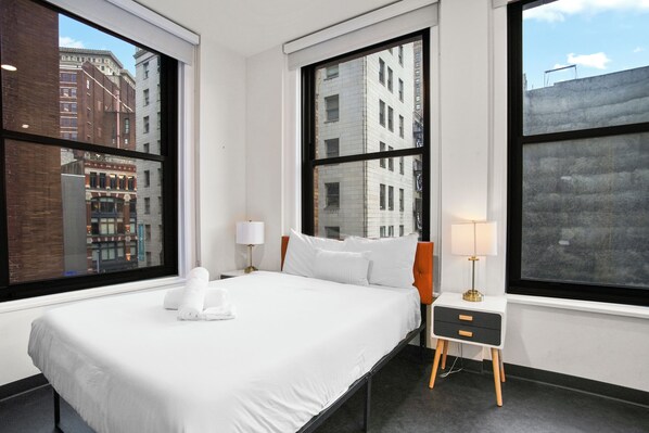 Une chambre d’hôtel avec un grand lit, deux tables de chevet et de grandes fenêtres donnant sur la ville.