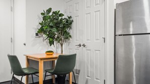 A small kitchenette with a wooden table, two chairs, a potted plant, and a stainless steel refrigerator. - CozySuites - William (Pittsburgh)