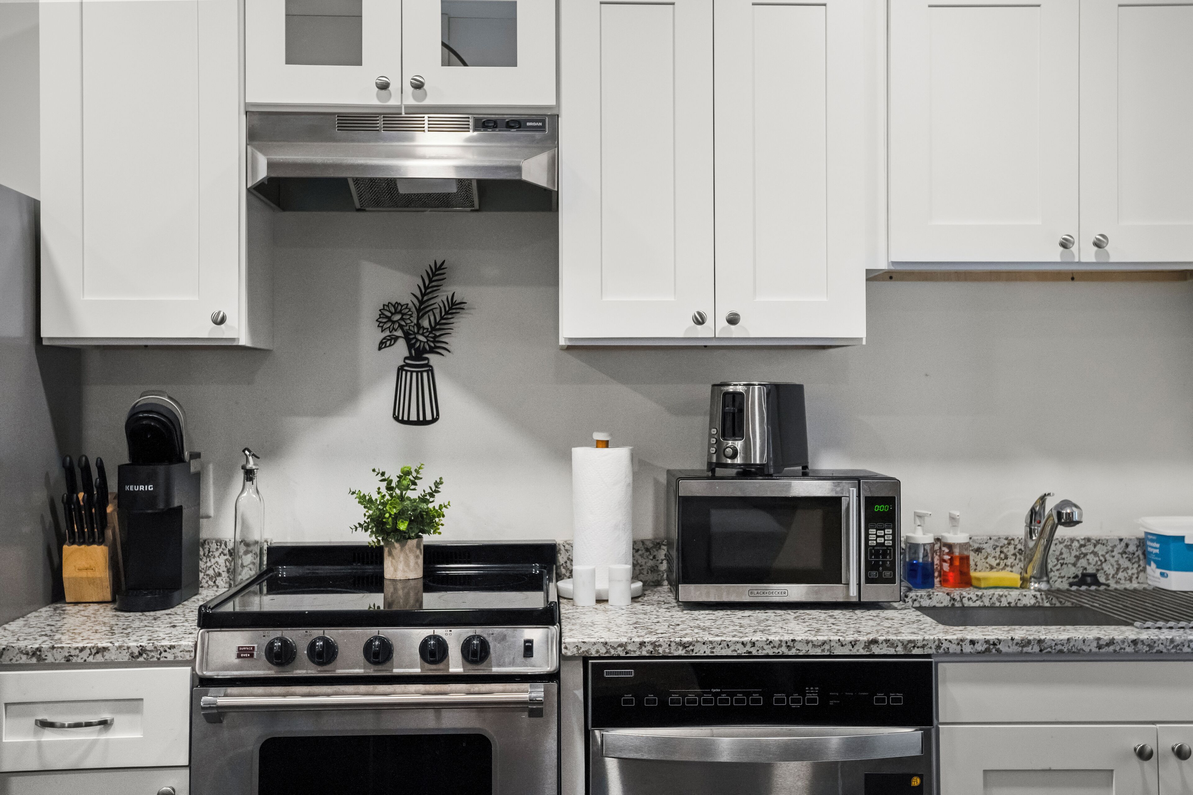 A modern kitchen with white cabinets, a stainless steel stove, a microwave, and a dishwasher.