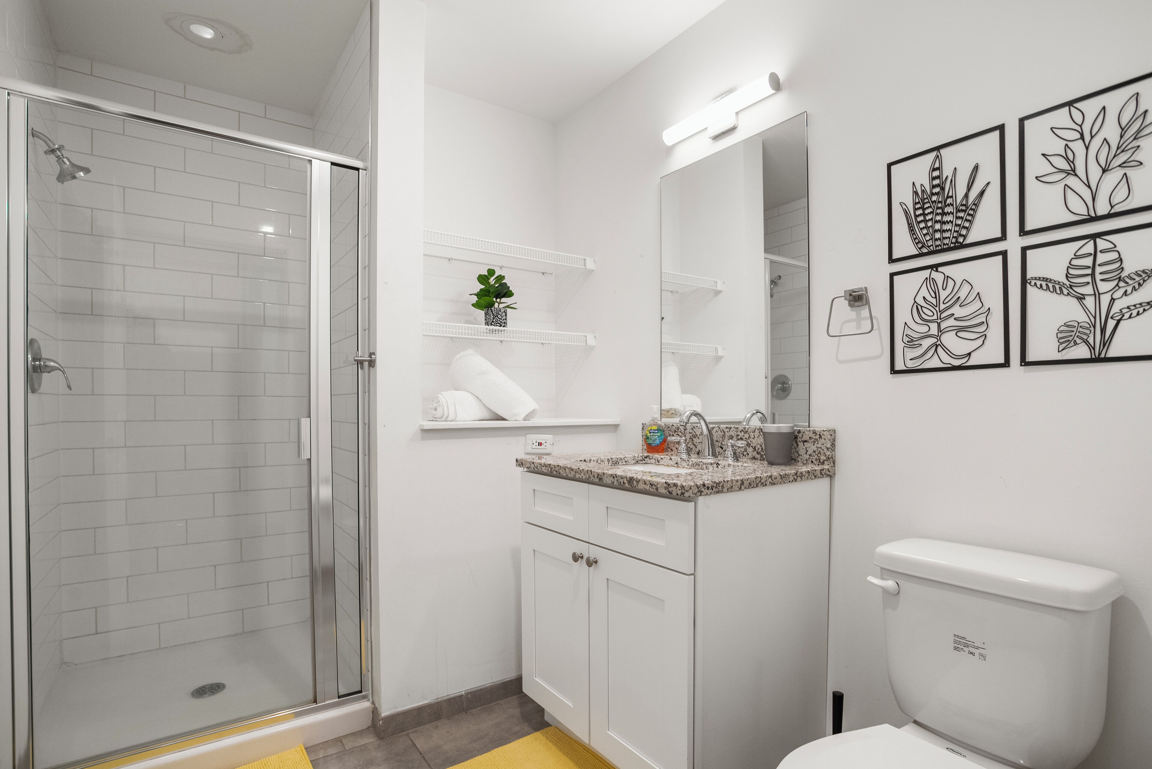 A modern bathroom with a glass shower enclosure, white cabinetry, a granite countertop sink, and a toilet.