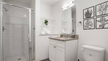A modern bathroom with a glass shower enclosure, white cabinetry, a granite countertop sink, and a toilet.