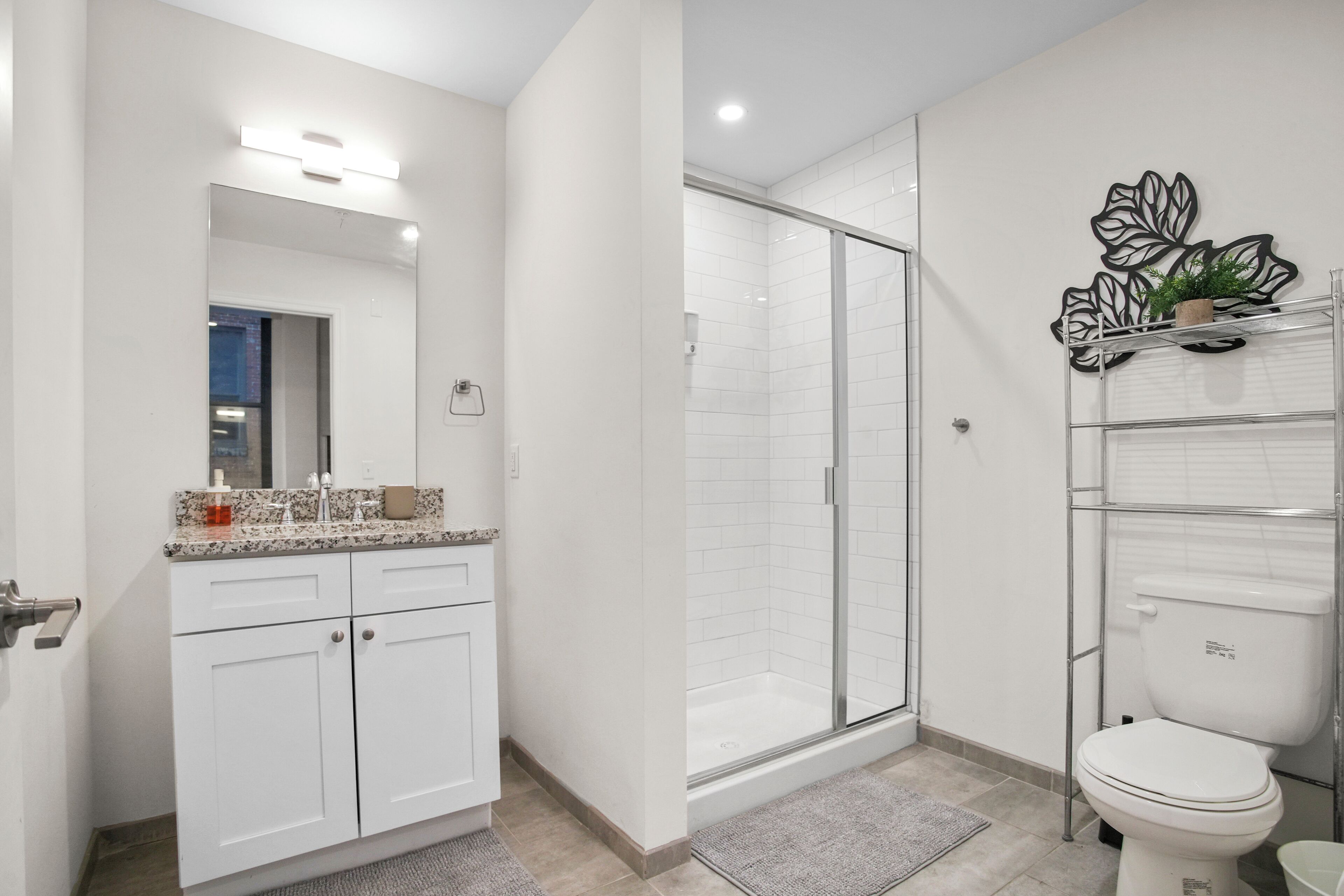 A modern bathroom with a glass shower enclosure, white cabinetry, and a toilet with a shelf above it.