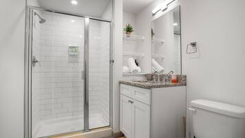 A modern bathroom with a glass-enclosed shower, white tiled walls, a granite countertop, and a toilet.