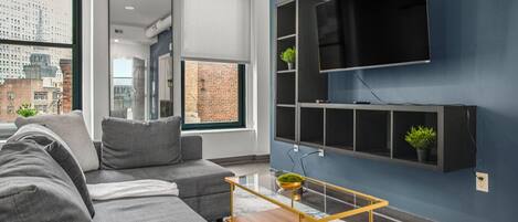 A modern living room with a grey sofa, a wooden coffee table, and a mounted TV on a blue wall.