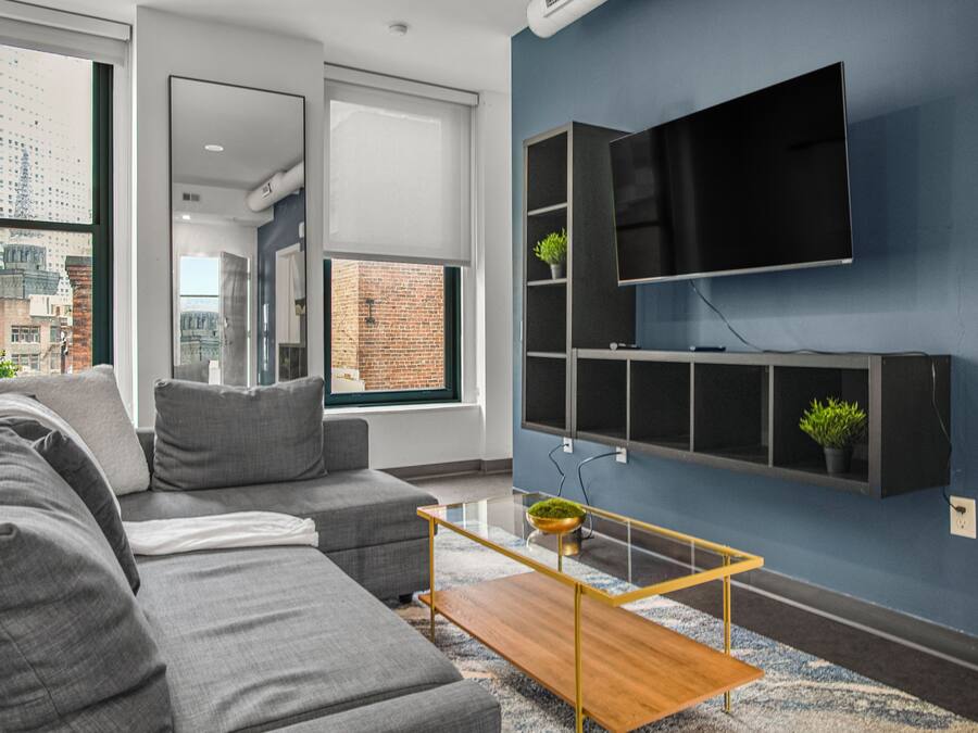 A modern living room with a grey sofa, a wooden coffee table, and a mounted TV on a blue wall.