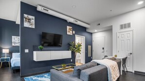 A modern living room with a grey sofa, a flat-screen TV mounted on the wall, a small coffee table, and a blue rug. - CozySuites - William (Pittsburgh)