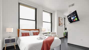 A modern hotel room with a large bed, bedside tables, a mounted TV, and large windows.