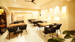 Un restaurant avec des tables en bois et des chaises noires, un ventilateur de plafond et des lampes fixées au mur.