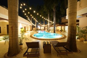 A pool area with lounge chairs and string lights, surrounded by palm trees and a building with multiple levels. - Bharti Forest Retreat (Tala)