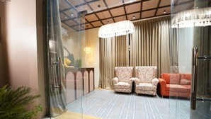 Un intérieur moderne avec une cloison en verre, deux fauteuils à motifs, un canapé rouge et un tapis à motifs.