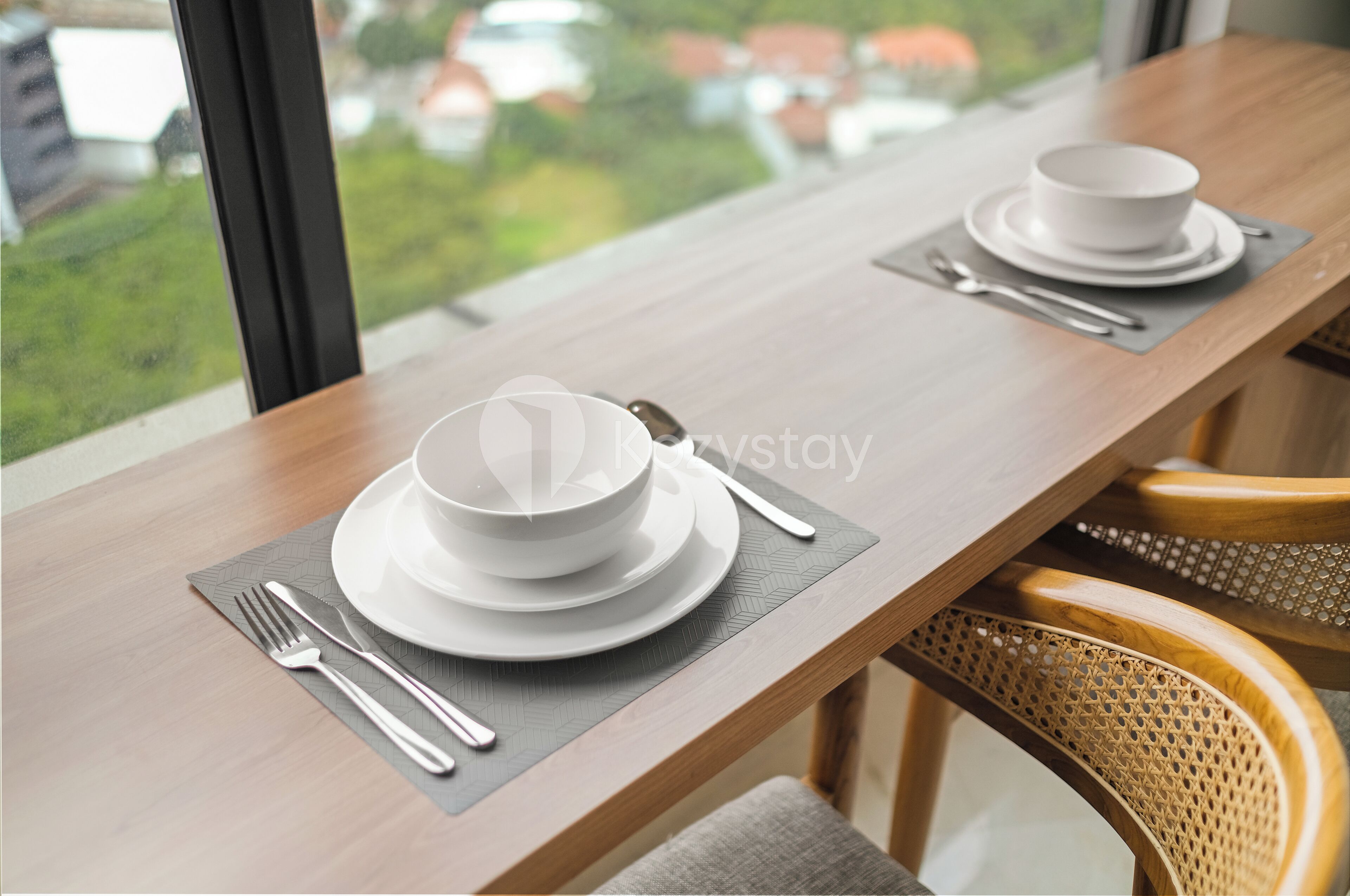 A dining table with white plates and cutlery, set with a placemat.
