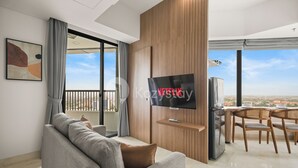 A modern living room with a grey sofa, a flat-screen TV, a wooden TV stand, and a dining area with wooden chairs. - Tenui by Kozystay - Tanjung Barat (Jakarta)