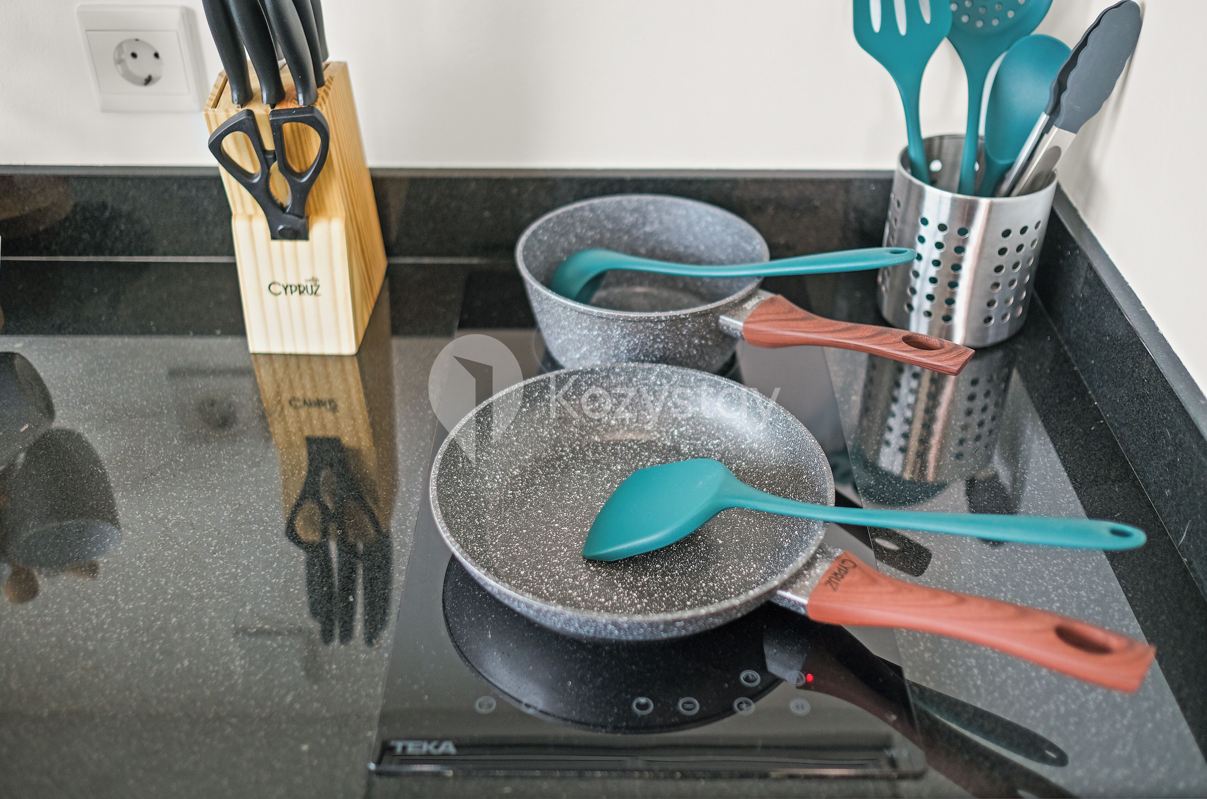 A kitchen with a frying pan on an induction cooktop, a wooden knife block, and a utensil holder with spatulas and a knife.