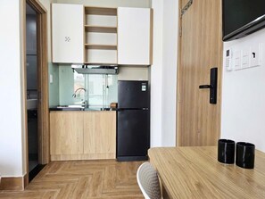A compact kitchen with a black refrigerator, wooden cabinets, and a small dining table with two black cups. - HOA PHU Hotel (Ho Chi Minh City)