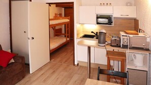 Una cocina compacta equipada con microondas, tostadora y tetera, una litera, y un pequeño comedor con mesa y sillas.