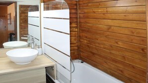 Un baño con pared de madera, un lavabo blanco y una bañera.