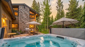 A hot tub with a stone wall and a wooden deck, surrounded by trees and a house with a stone facade. - Fire and Ice/Northstar Resort Truckee, CA (Truckee)