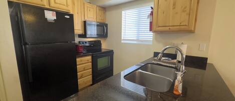A kitchen with wooden cabinets, a black refrigerator, a microwave, a stove, and a sink.