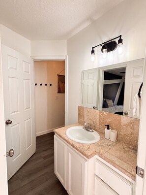 Une salle de bain avec un lavabo blanc, un miroir et un luminaire placé au-dessus.