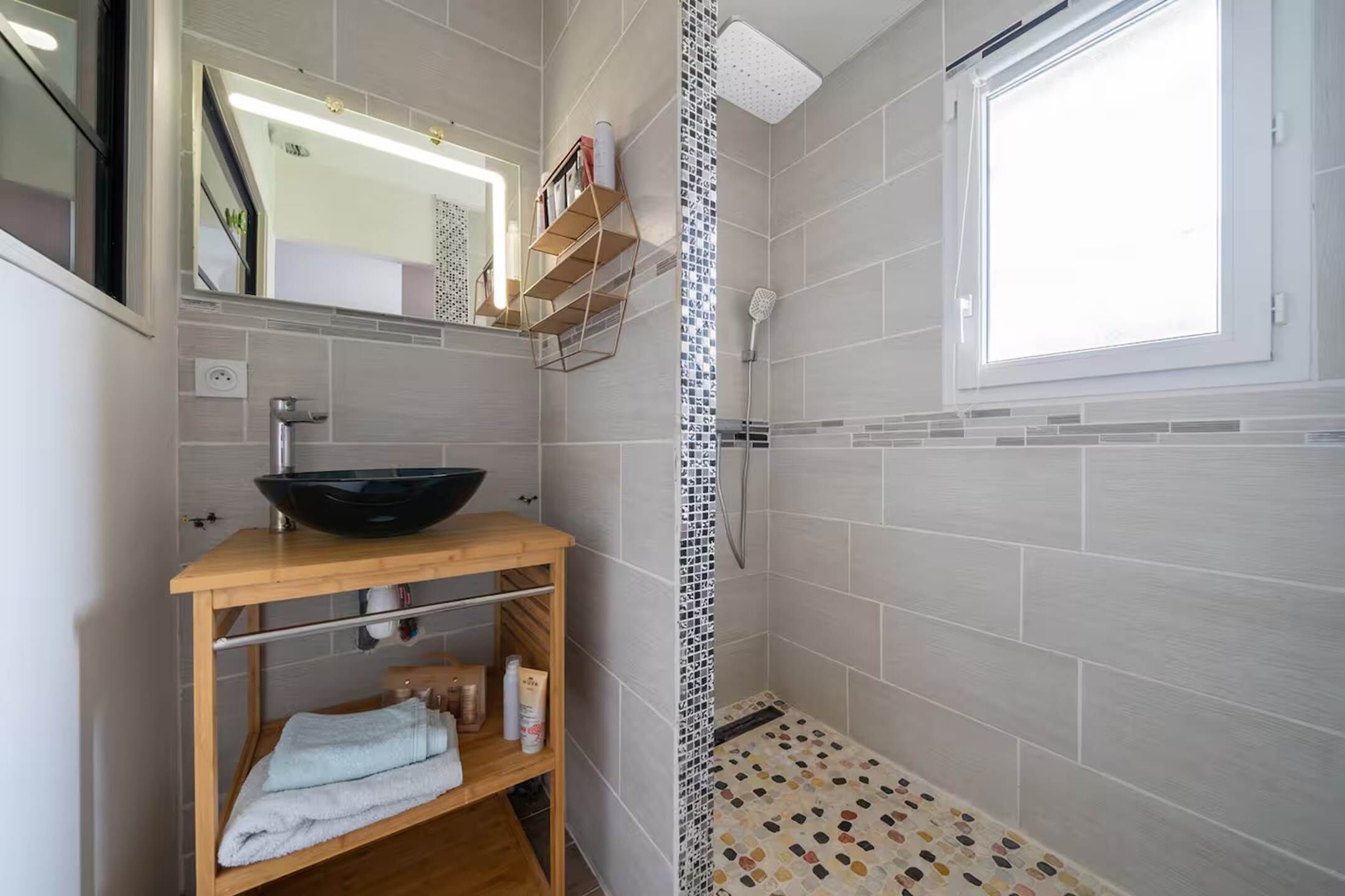 A bathroom with a modern sink, a shower, and a window.