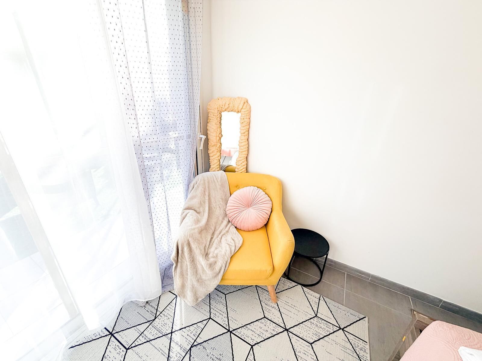 Une pièce avec un fauteuil jaune, un lampadaire noir et un tapis à motifs.