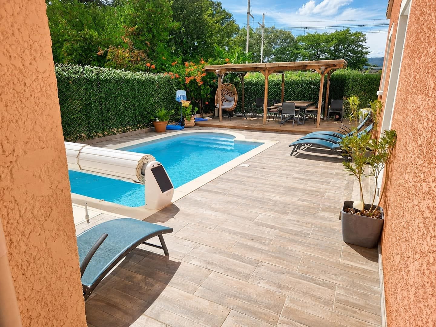 Ein Swimmingpool mit einer Holzterrasse, Liegestühlen und einer Pergola.